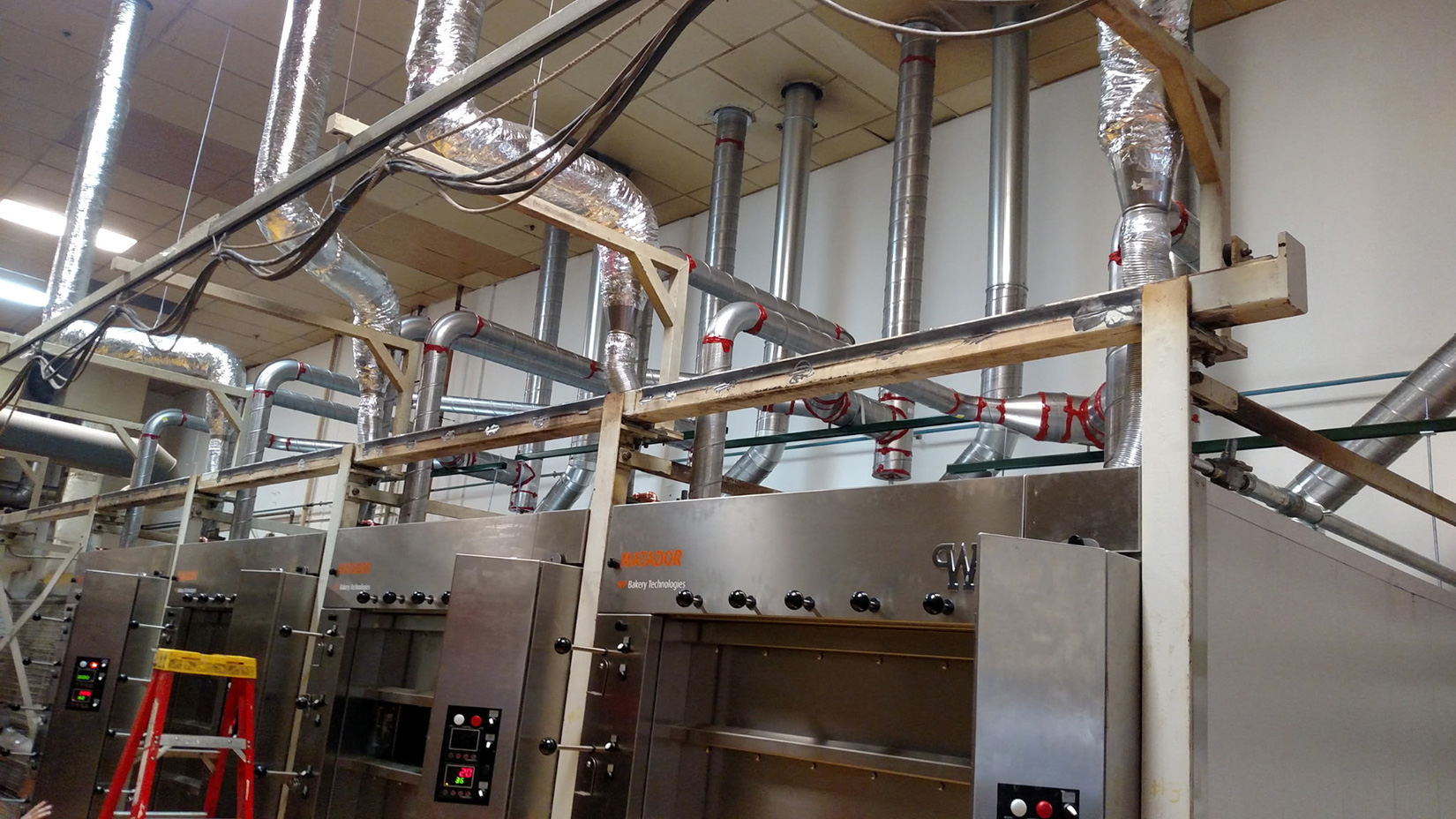 Commercial bakery ventilation ductwork and mechanical exhaust system installed above baking equipment.