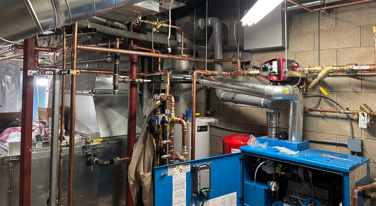 Commercial boiler room with copper piping, pumps, ductwork, and mechanical equipment.