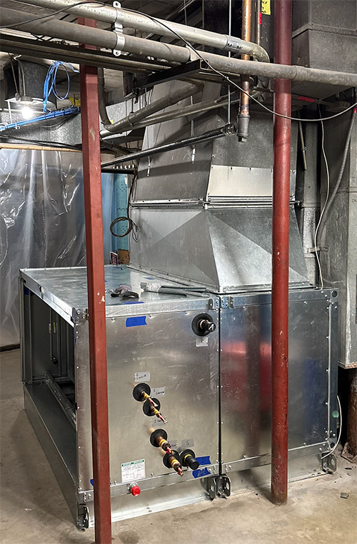 Commercial HVAC air handling unit connected to ductwork and piping.