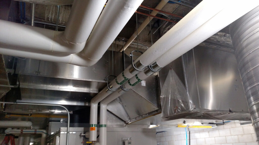 Commercial mechanical piping and ductwork installed above a building workspace.