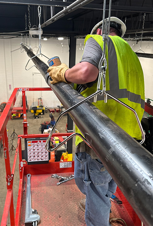 Commercial pipefitter installing large black pipe from an elevated lift.