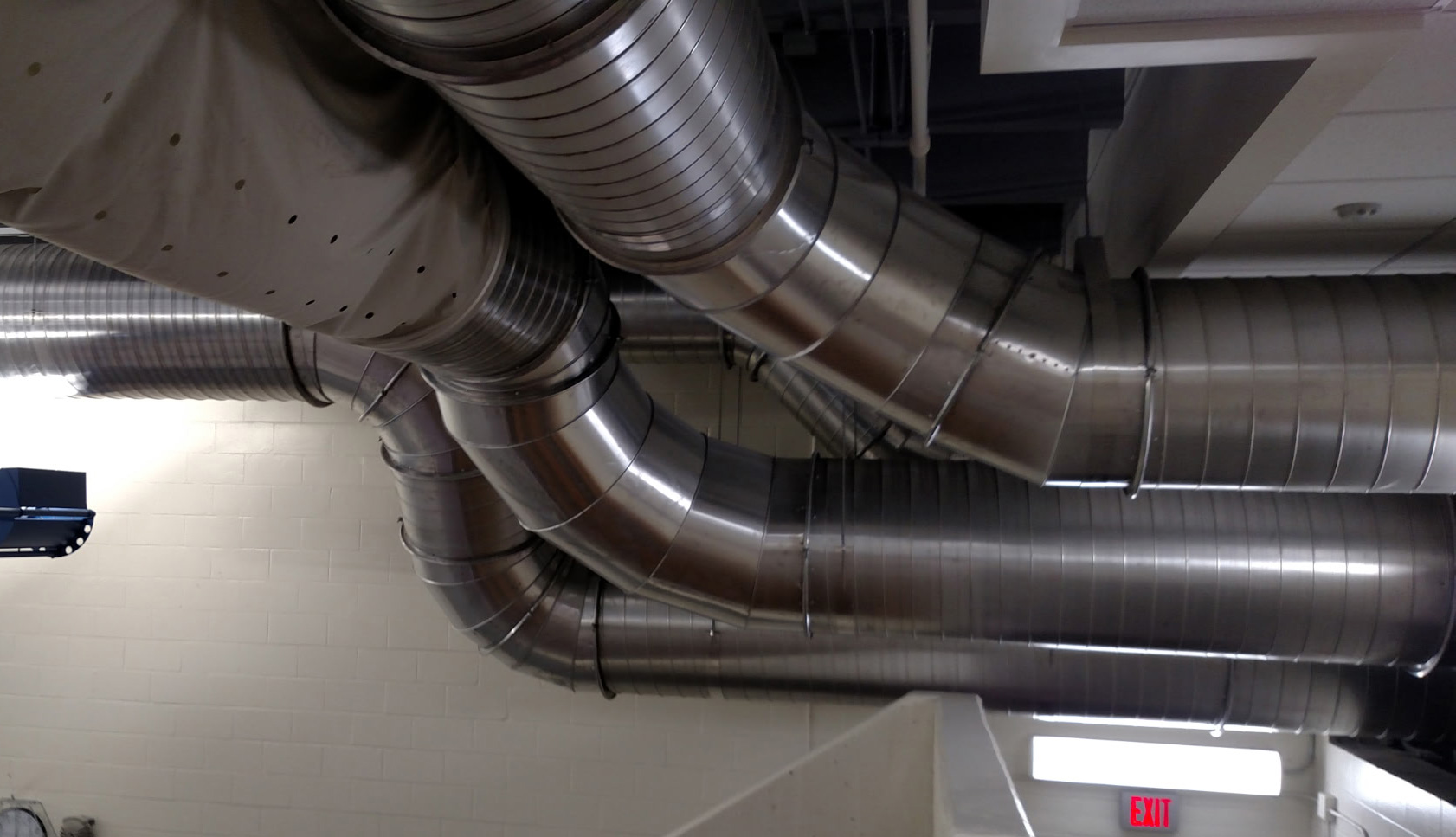 Round commercial ductwork and ventilation connections inside a mechanical space.