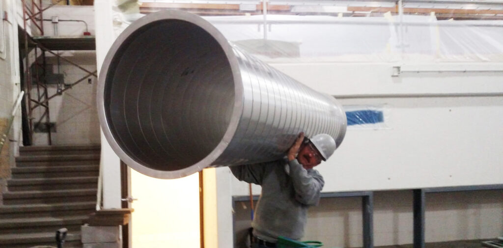 Sheet metal worker carrying large round ductwork for commercial HVAC installation.